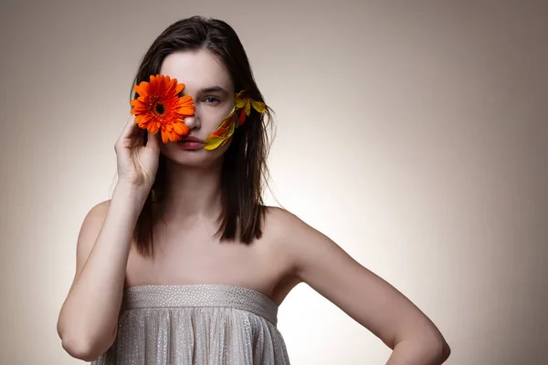 Hermosa modelo escondiendo la mitad de su cara con flor naranja —  Fotos de Stock