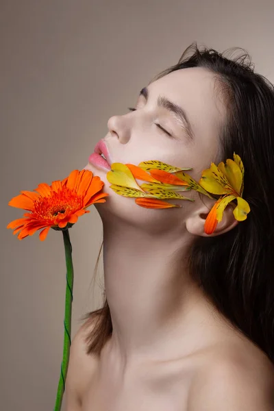 Model with petals on face and flower in hands closing eyes