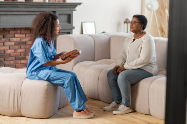 Yaşlı bayan kanepede oturan ve özel hemşire nin sorularını yanıtlayan