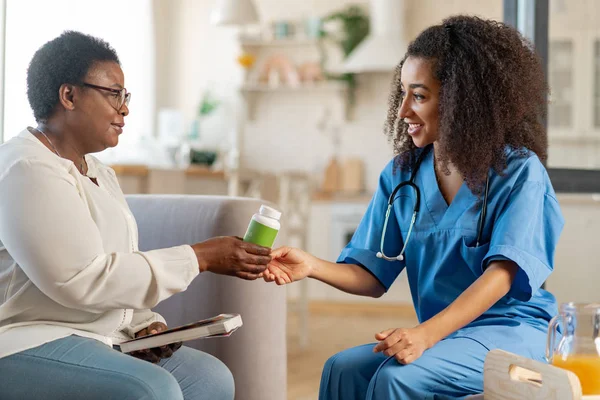 Thankful aged woman taking pills from caring medical attendant — Stock Photo, Image