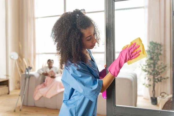 Curly verzorger reiniging van de glazen deur thuis van de patiënt — Stockfoto