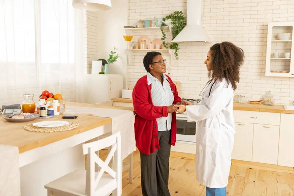 Woman wearing red cardigan feeling grateful to pleasant nurse — Stock Photo, Image