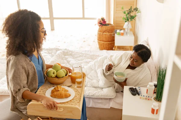 Zorgzame krullend verpleegster met dienblad met ontbijt voor patiënt — Stockfoto