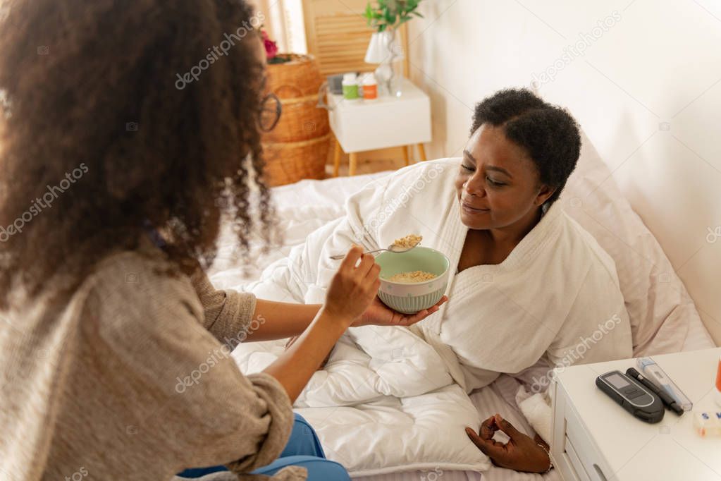 Nurse giving some porridge for woman lying in bed after surgery