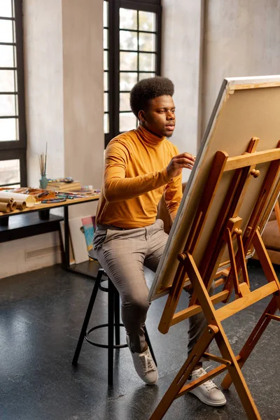 Miły utalentowany człowiek siedzi przed jego malarstwo — Zdjęcie stockowe
