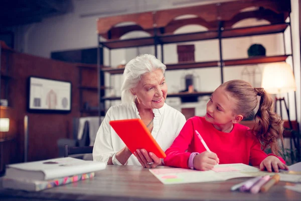 Grey-haired cute granny coloring pictures with granddaughter — Stock Photo, Image