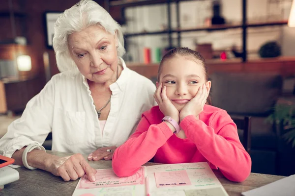 Cheerful cute girl feeling funny while doing homework with granny — Stock Photo, Image