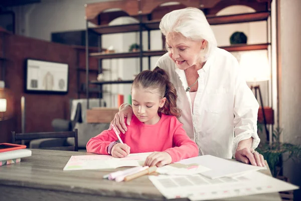 Caring grey-haired granny hugging her cute girl writing letters — Stock Photo, Image