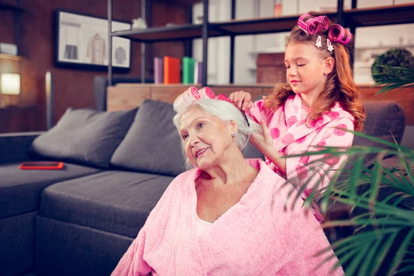 Cute girl with hair rollers brushing hair of her lovely grandmother — Stock Photo, Image