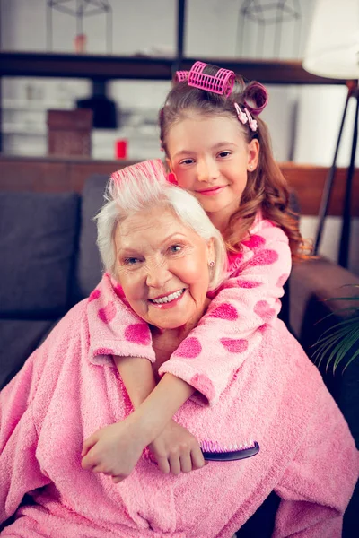 Granny and girl wearing bathrobes curling their hair with rollers — Stock Photo, Image