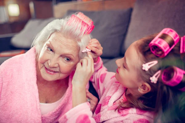 Lovely cute girl putting hairpin on hair of her beautiful granny