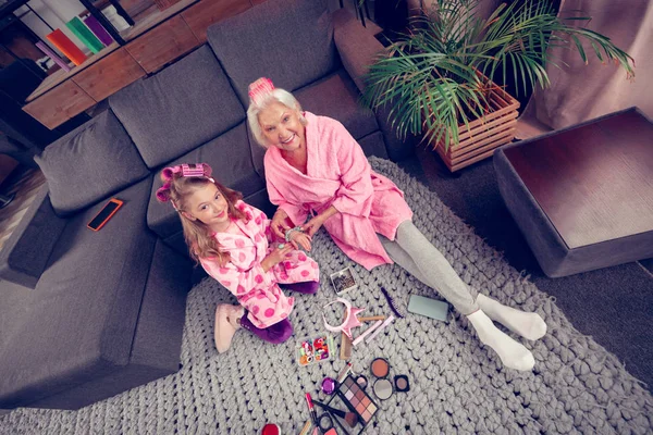 Cute girl and granny sitting on floor before doing makeup