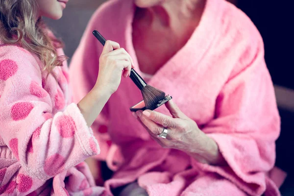Mädchen und ihre Oma tragen rosa Bademäntel und nehmen Gesichtspuder — Stockfoto