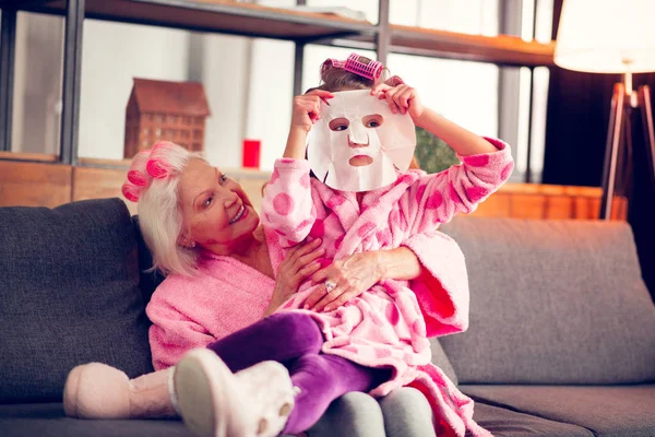 Дівчина відчуває себе допитливою під час спроби листової маски сидіти біля бабусі — стокове фото