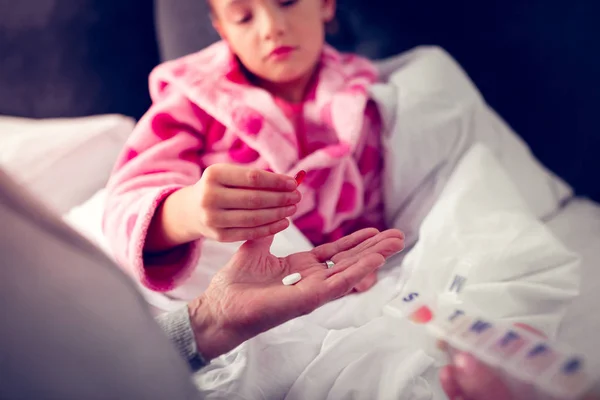 Girl in pink bathrobe taking pills from granny while feeling sick