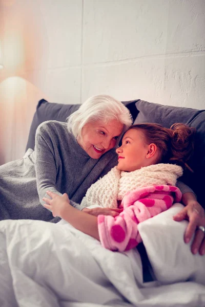 Caring granny hugging her cute girl staying in bed feeling sick