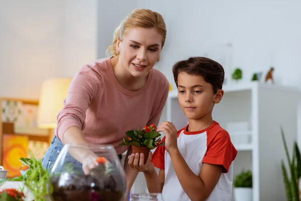 Aluno segurando vaso com flores vermelhas de pé perto professor — Fotografia de Stock