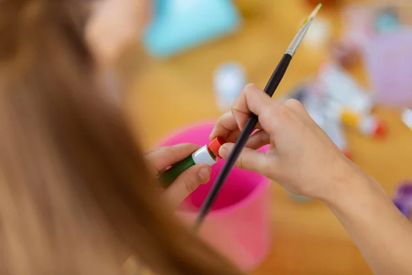 Close up de menina segurando pintura escova abertura guache tubo — Fotografia de Stock