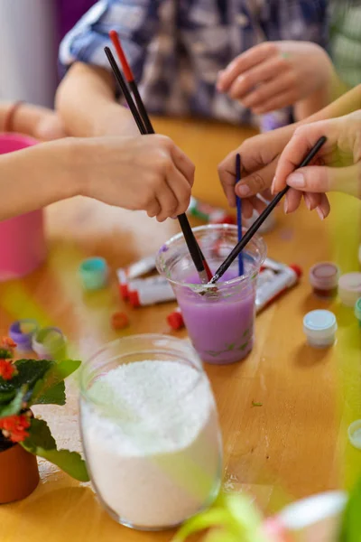 Pupils and teacher putting painting brushes into purple gouache