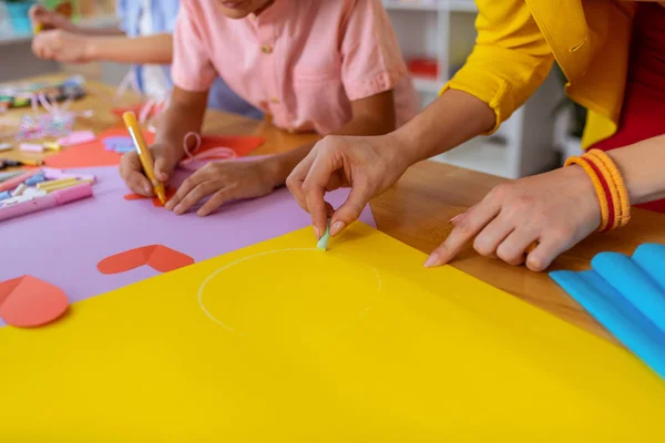 Lärare som hjälper eleverna att måla cirkel på gult papper — Stockfoto