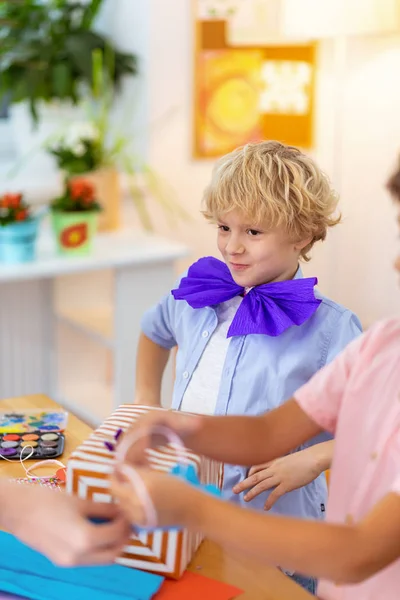 Blonde schoolboy wearing blue paper bow at the art lesson — Stock Photo, Image