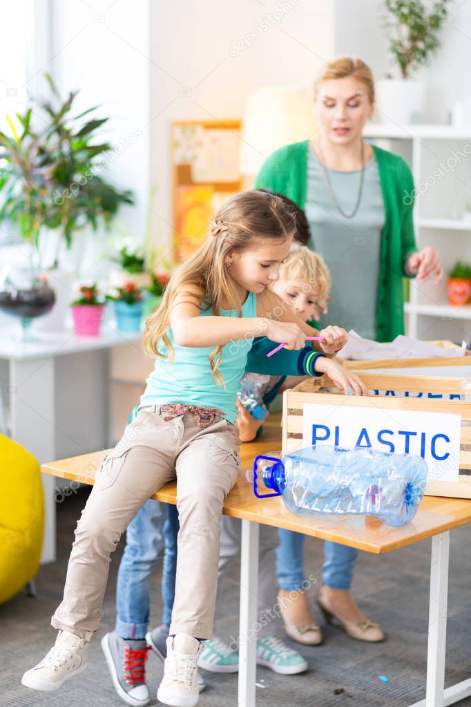 Girl sitting on table at school and sorting plastic with classmate