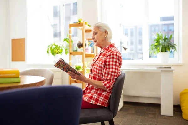 Trevlig åldrad kvinna läser en bok hemma — Stockfoto