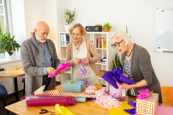 Joyful elderly people enjoying wrapping their gifts