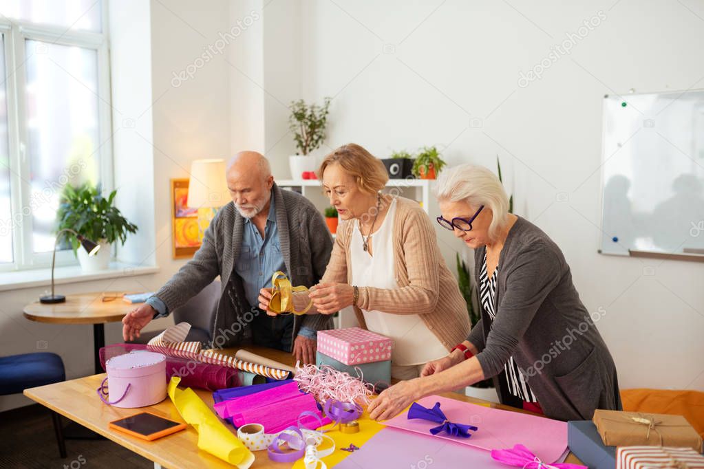 Pleasant nice aged people wrapping gifts together