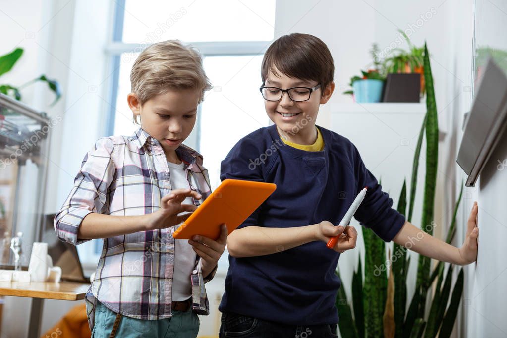 Beaming good-looking young boys carrying tablet and marker