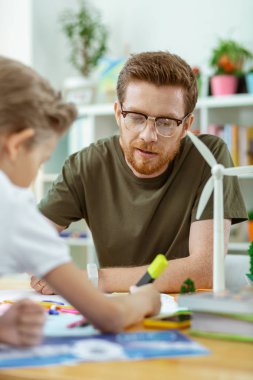 Poster üzerinde çalışan odaklanmış iyi görünümlü zencefil öğretmeni