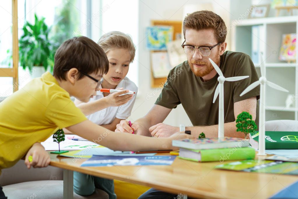 Concentrated bearded teacher spending time with his curious pupils