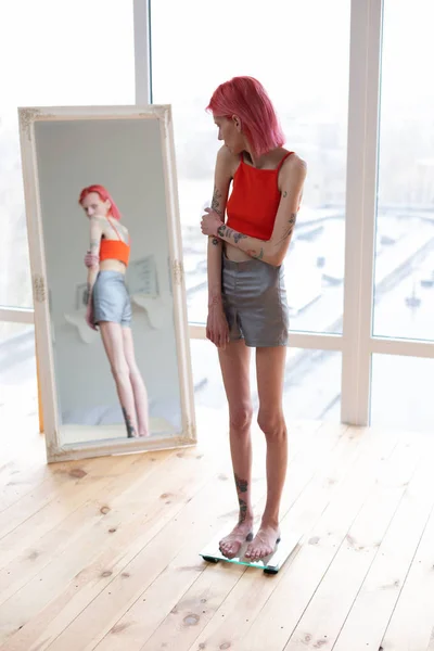 Anorexic woman standing on scales and looking into mirror