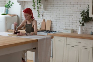 Geniş mutfakta oturan ve çikolatalı pastaya bakan bir kadın.