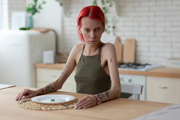 Anorexic woman having awful look sitting in the kitchen