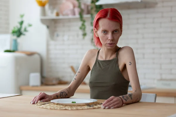 Roodharige anorexische vrouw die alleen in de keuken zit — Stockfoto