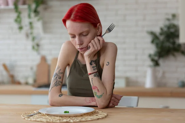 Vrouw met boulimia vork en kijkend naar bord met erwten — Stockfoto