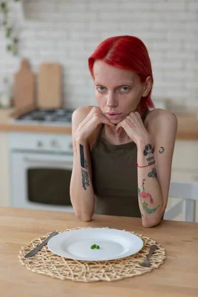 Vrouw met anorexia zittend in de keuken met leeg bord — Stockfoto