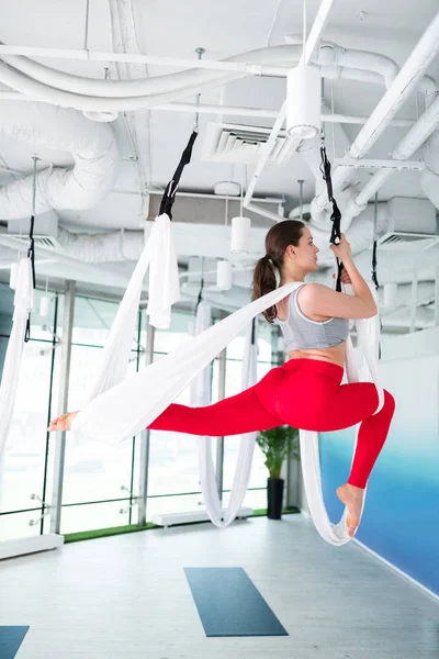 Slim and active woman in red leggings doing aerial yoga
