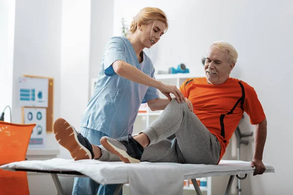 Mulher loira agradável tocando seu joelho pacientes — Fotografia de Stock