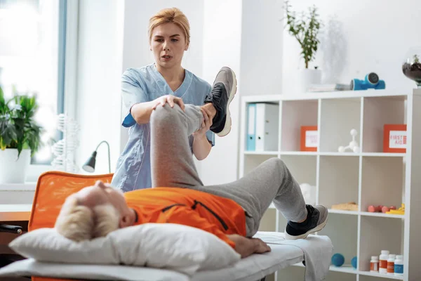 Mujer rubia agradable sosteniendo sus pacientes pierna — Foto de Stock