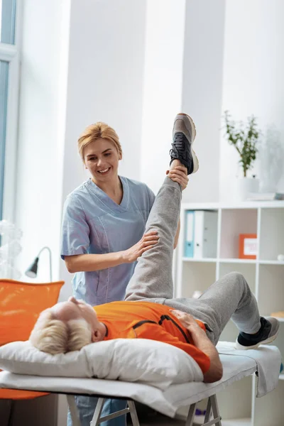 Enfermeira profissional alegre levantando seus pacientes perna para cima — Fotografia de Stock