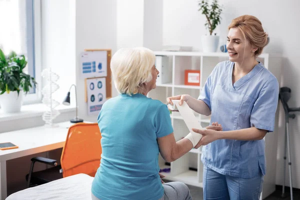 Позитивная дружелюбная медсестра, стоящая рядом с пациентом — стоковое фото