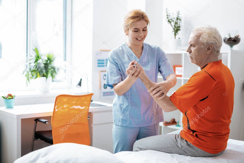 Joyful positive woman massaging her patients hand