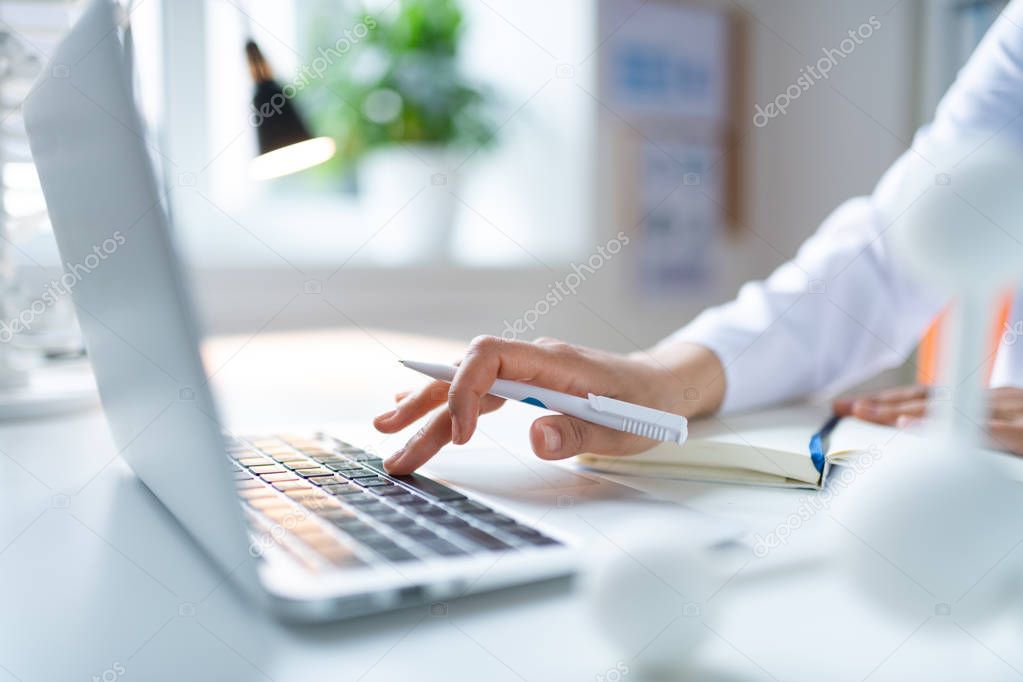 Close up of female chemist holding white pen using laptop