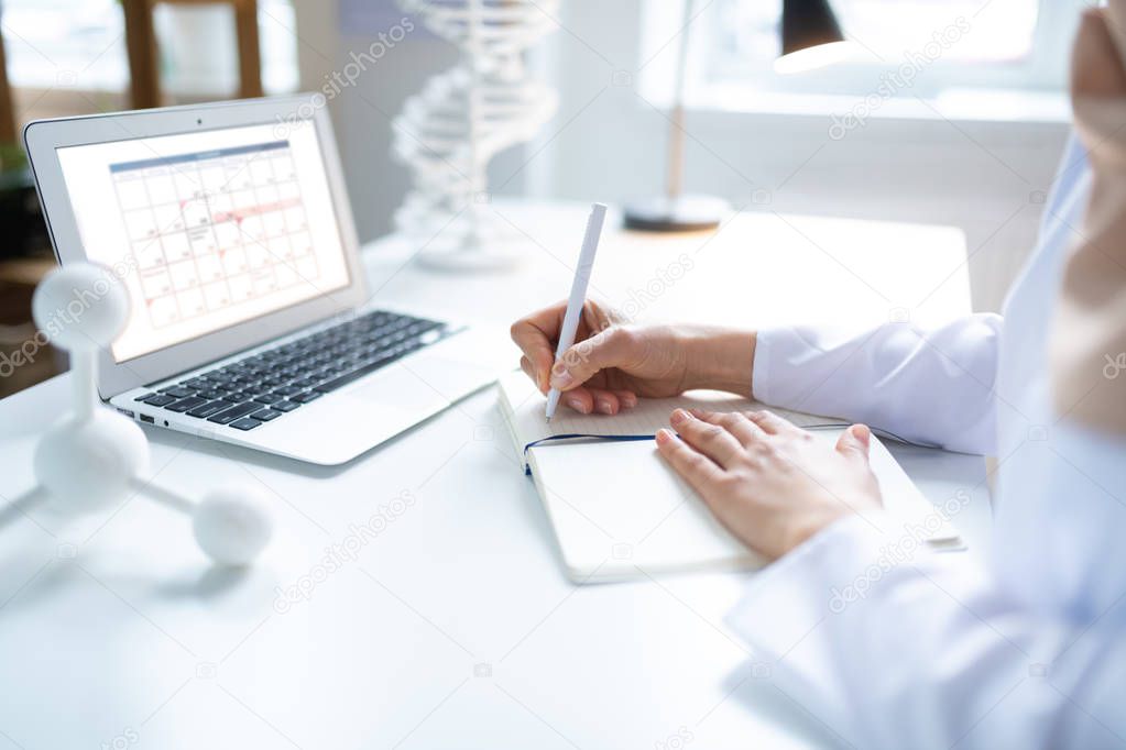 Scientist checking her schedule on laptop while making notes