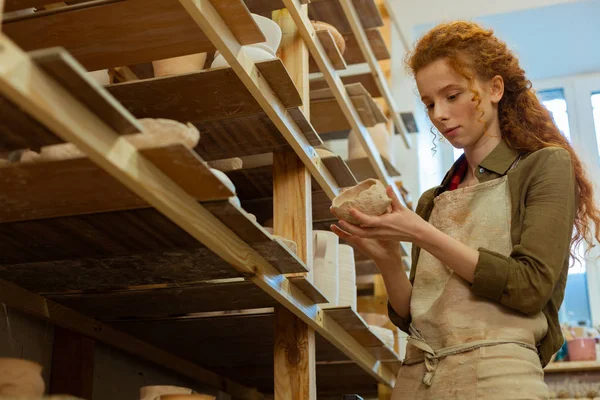 Focused ginger master in protective apron holding unusual clay pot — Stock Photo, Image