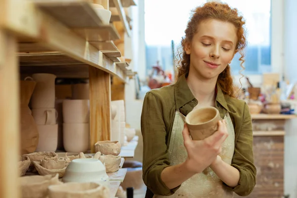 Smiling long-haired curly lady attentively observing clay pot