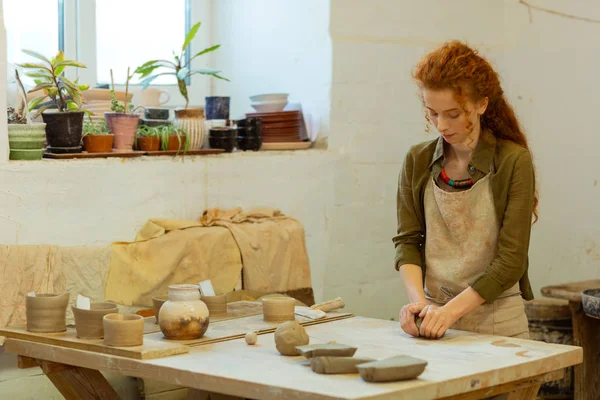 Concentrated long-haired ginger girl intensely warming fresh clay — Stock Photo, Image