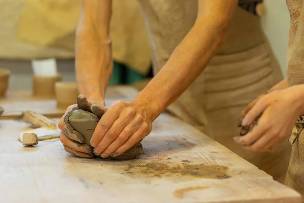 Sterke man strak persen stukje verse klei op een houten tafel — Stockfoto